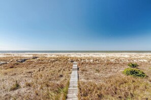 Une promenade en bois qui mène à une plage bordée de dunes de sable et dotée d’une végétation clairsemée.