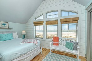 Une chambre à coucher avec un lit, une chaise et de grandes fenêtres donnant sur une plage.