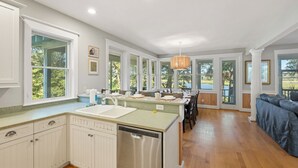 Una cocina amplia con una isla central, ventanas grandes y una zona de comedor con un sofá azul.