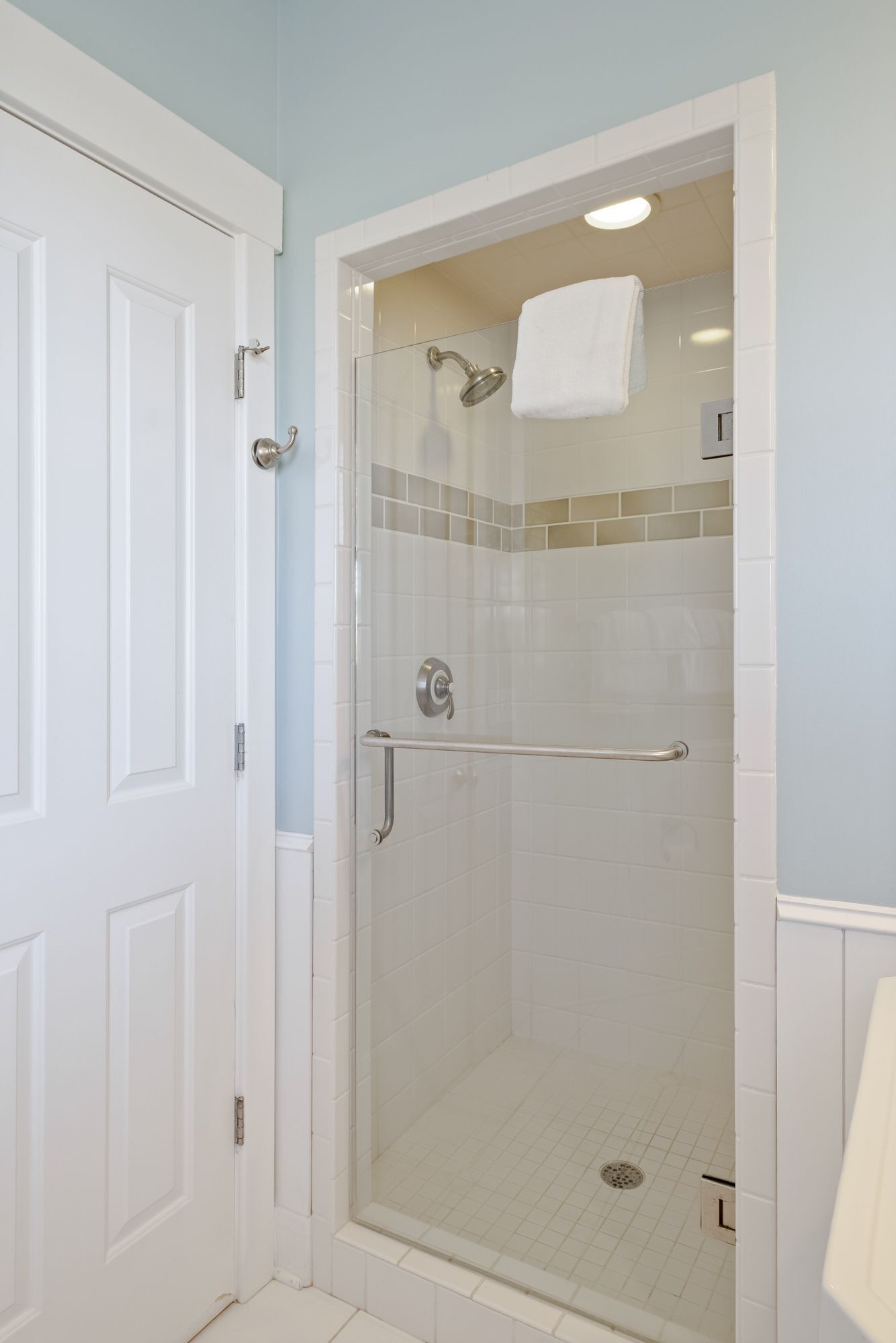 A walk-in shower with a glass door, a handrail, and a white towel hanging on the wall.
