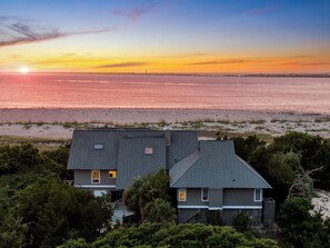A two-story house with a dark roof and light walls, surrounded by dense greenery and a beach. - Poolside Paradise is luxury vacationing! Enjoy beautiful sunsets (Bald Head Island)