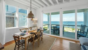 A dining area with a table set for four, a hanging light fixture, and a view of the sea through large windows. - Welcome to one of the Island (Bald Head Island)