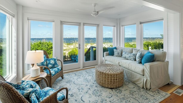A sunroom with a view of the ocean, wicker furniture, and a large sofa with blue cushions. - Welcome to one of the Island (Bald Head Island)