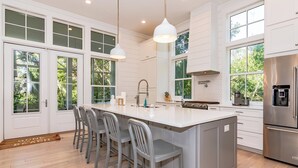 A modern kitchen with a large island, bar stools, and a stainless steel refrigerator. - Your dream vacation retreat is nestled in the Maritime Forest (Bald Head Island)