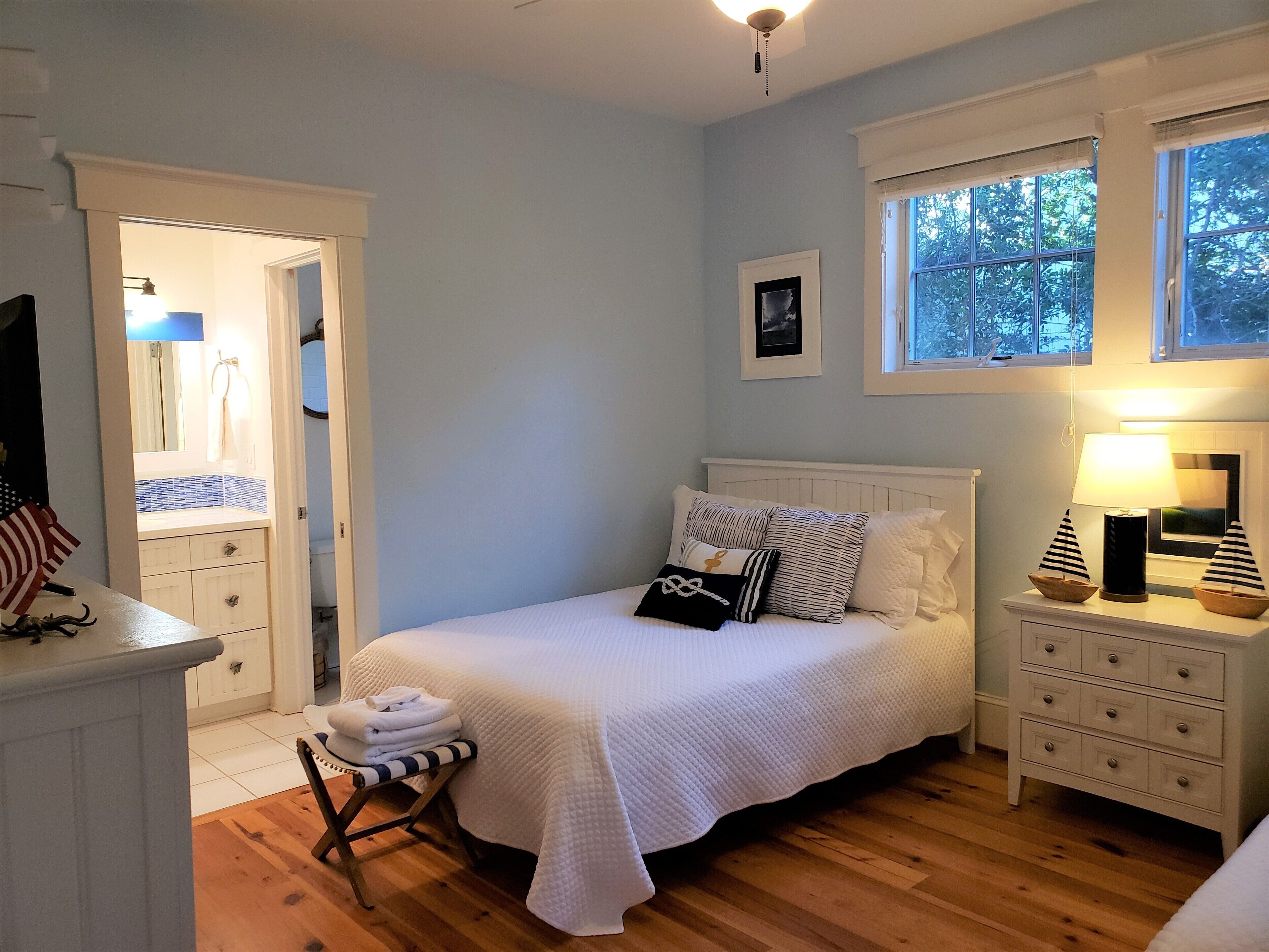 Un dormitorio con cama, mesitas de noche, una ventana y una puerta que da al baño.