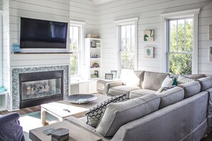 A living room with a fireplace, a sofa, a coffee table, and a TV mounted on the wall. - Moondance delights with its designer touches! (Bald Head Island)