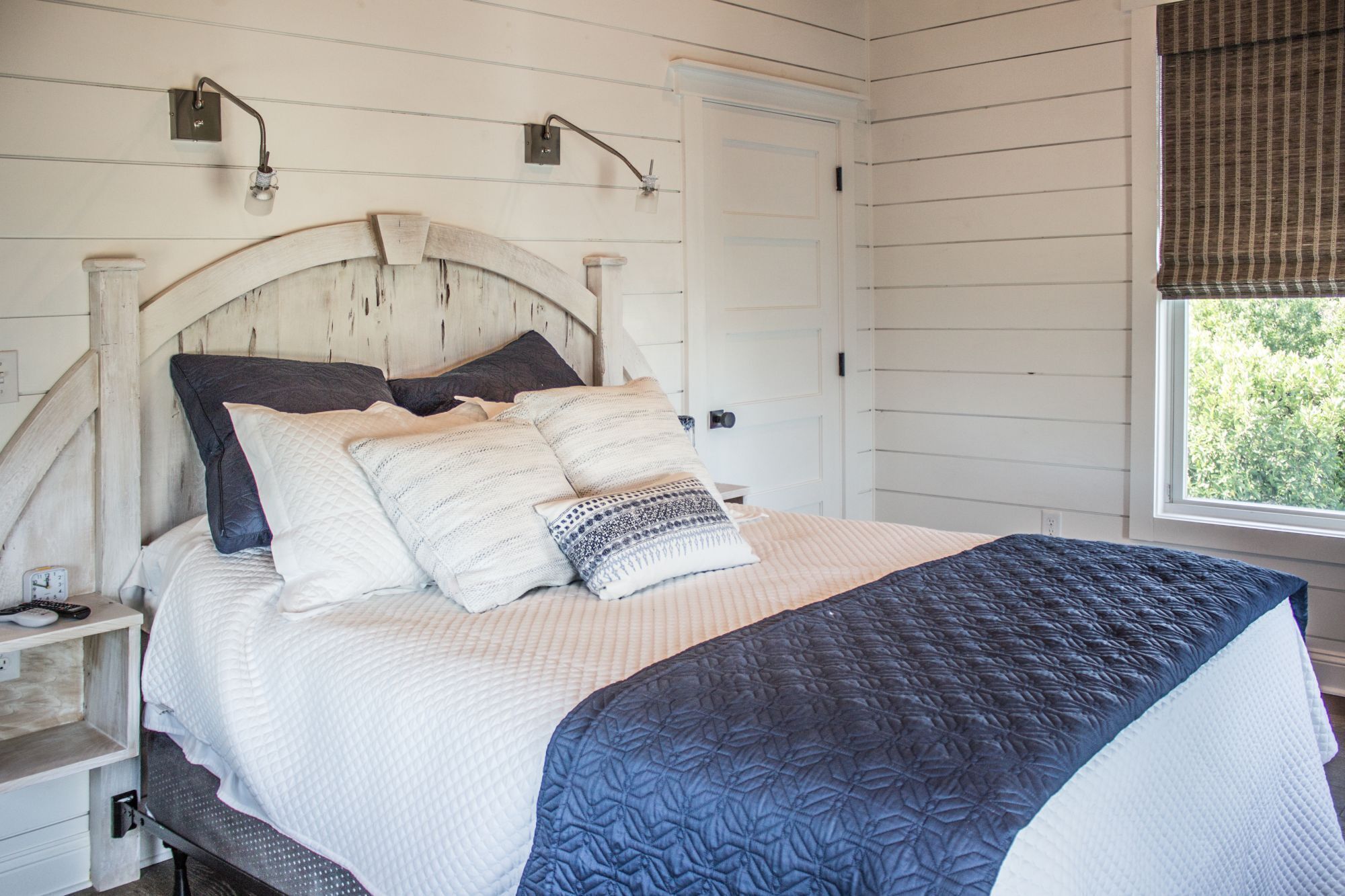 A bedroom with a bed, bedside tables, a window with a view, and a door.