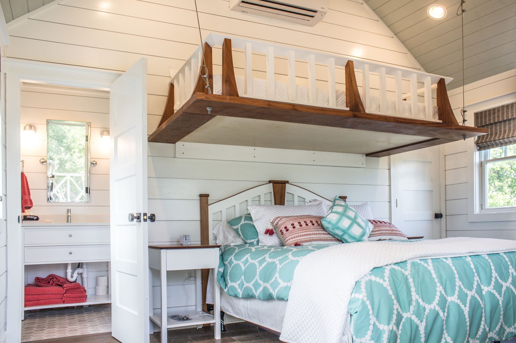Une chambre avec un lit superposé, une coiffeuse avec un miroir et une fenêtre donnant sur les arbres.