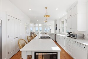 A modern kitchen with white cabinetry, a central island, and a view to the outside. - Executive Retreat HAS IT ALL-privacy, beach proximity (Bald Head Island)