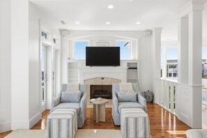 A spacious living room with a fireplace, two sofas, a television, and large windows. - Executive Retreat HAS IT ALL-privacy, beach proximity (Bald Head Island)