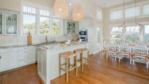 A spacious kitchen with white cabinetry, a large island, and a dining area with white chairs. - Captain Tank's Ocean View with covered deck (Bald Head Island)