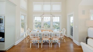 A spacious dining area with a large table and chairs, large windows, and a view of the outdoors. - Captain Tank's Ocean View with covered deck (Bald Head Island)