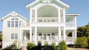 A two-story house with a balcony, a covered porch, and a garage. - Captain Tank's Ocean View with covered deck (Bald Head Island)