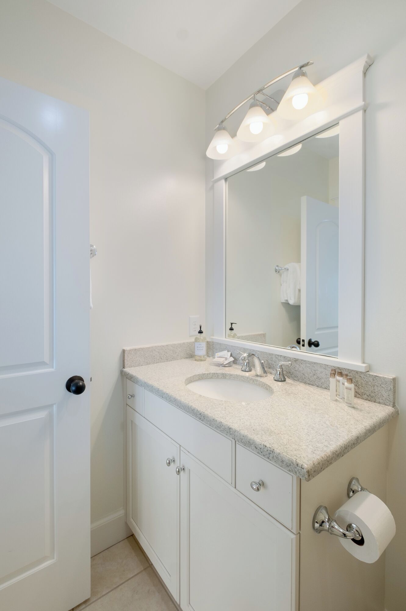 A bathroom with a white door, a sink with a mirror above it, and a toilet paper holder.