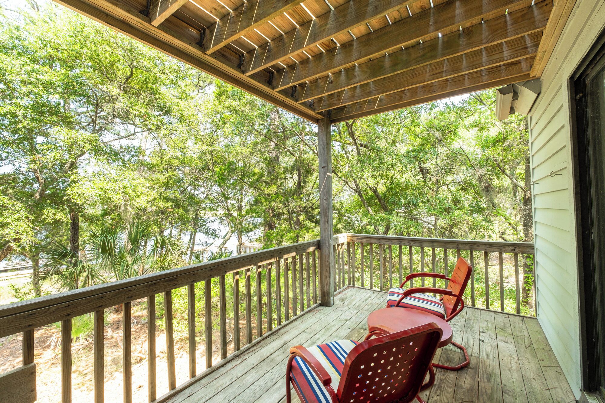 Une terrasse en bois avec une rambarde, deux chaises rouges dotées de coussins à rayures, et une vue sur les arbres.