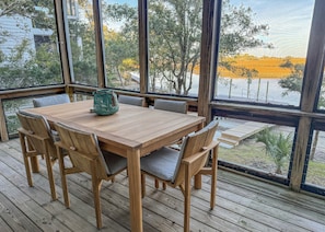Eine Holzterrasse mit Tisch und Stühlen, große Fenster mit Blick auf Bäume und ein Feld.