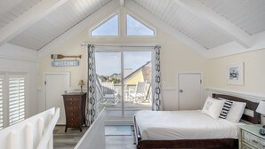 Ein Schlafzimmer mit schrägen Wänden, einem Bett, einer Kommode und Blick auf die Terrasse.