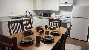 A modern kitchen with white cabinets, a wooden dining table set with plates and cups, a microwave, and a refrigerator. - Spacious home w/dual entrance for added privacy. Near HMT system, dining & shops (Logan)