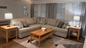 A living room with a sectional sofa, two side tables with lamps, a coffee table, a ceiling fan, and a window with curtains. - Spacious home w/dual entrance for added privacy. Near HMT system, dining & shops (Logan)