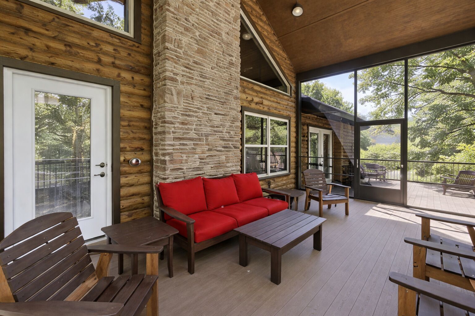 A log cabin interior with a red sofa, wooden benches, and a balcony with outdoor seating.