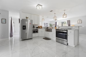 A modern kitchen with white cabinets, stainless steel appliances, and pendant lighting.