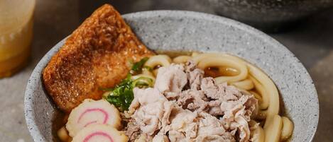A bowl of ramen with various toppings, a cup of iced coffee, and a plate of food in the background.