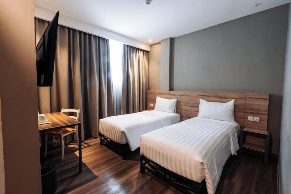 A hotel room with two beds, a desk, and a TV.