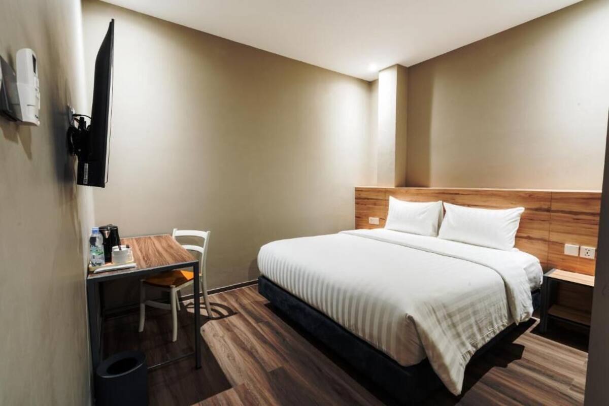 A hotel room with a bed, a desk, a chair, and a television mounted on the wall.