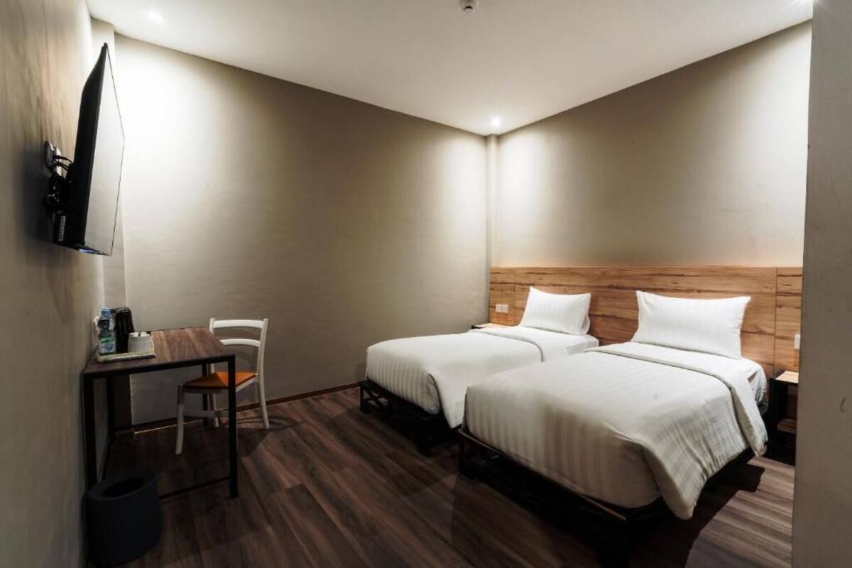 A hotel room with two beds, a desk with a chair, a TV mounted on the wall, and a wooden headboard.