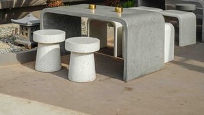 A modern outdoor seating area with concrete tables and stools, surrounded by greenery and a building facade. - STAY KERTAPATI HOTEL (Palembang)