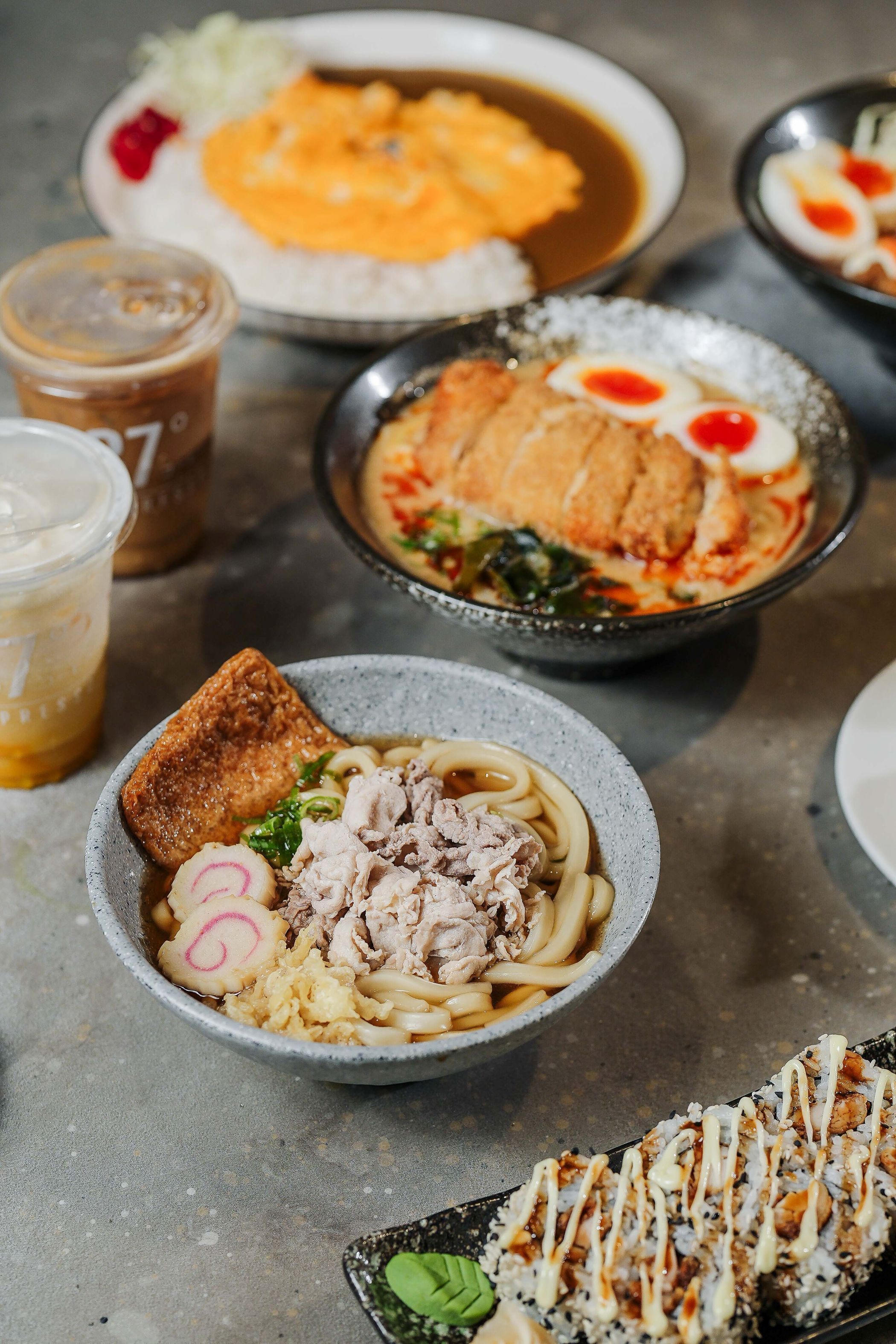 A variety of dishes including ramen, sushi, and a cup of iced coffee.