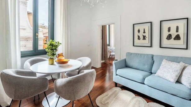 En moderne stue med en blå sofa, et rundt spisebord med stole og en lysekrone.
