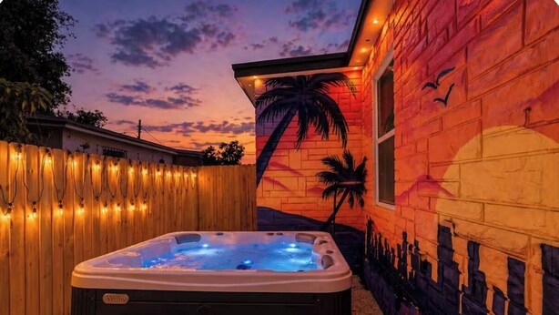 Ein Whirlpool in einem Garten mit Abendhimmel, Holzzaun und Wandmalerei von Palmen und einer Kuppel.
