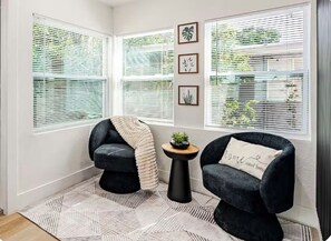 Une pièce comprenant deux fauteuils noirs, une petite table ronde ornée d’une plante et un tapis à motifs géométriques.