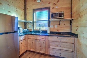 A kitchen with wooden cabinets, a stainless steel refrigerator, a microwave, and a window with blinds. - Cozy 1-bedroom 1- bath with queen sleeper sofa cabin in beautiful Cosby (Cosby)