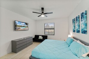 A bedroom with a bed, a TV, a ceiling fan, a window, and artwork on the wall. - Tide & Tee Retreat~Heated Pool~Canal Kayaks~Golf Course Views~Sleeps 10 (Cape Coral)