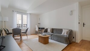 A modern living room with a grey sofa, a round coffee table, and a dining area with a table and chairs. - Blueground | Europe, view, nr Parc Monceau (Paris)