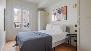 A bedroom with a bed, a window with a balcony, a bedside table, and a wall-mounted light fixture. - Blueground | Europe, view, nr Parc Monceau (Paris)