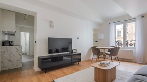 A modern living room with a flat-screen TV, a dining table with chairs, a sofa, and a kitchen area with a marble countertop. - Blueground | Europe, view, nr Parc Monceau (Paris)