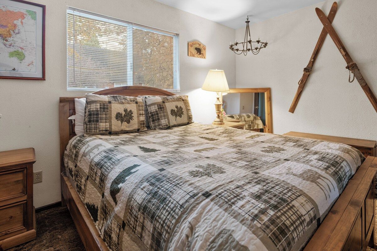 A bedroom with a bed, a nightstand, a lamp, a map on the wall, and a mirror.
