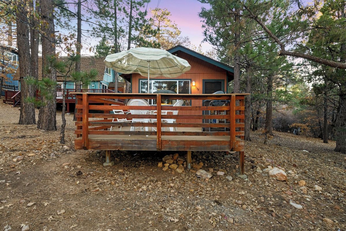 A cabin with a deck, outdoor seating, and a large umbrella.
