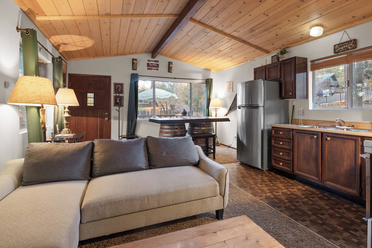 Una sala de estar acogedora con sofá, mesa de comedor y zona de cocina con armarios y refrigerador.