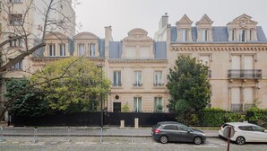 Een rij klassieke Europese herenhuizen met gelijke gevels, een kinderkopjesstraat en een zwart metalen hek op de voorgrond.