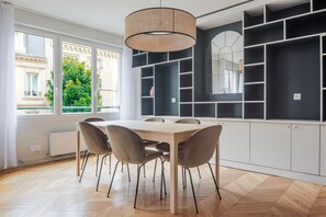 A modern kitchen with a wooden table and chairs, built-in black shelving, and a large window with a view of greenery. - Blueground | Paris, view, nr Parc de la Villette (Paris)