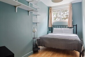 A bedroom with a bed, a bedside table, a lamp, and a window with curtains. - Blueground | Paris, view, nr Parc de la Villette (Paris)