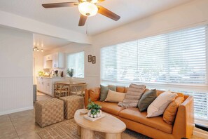 A living room with a brown leather sofa, ottomans, a coffee table, and a ceiling fan. - Bright Coastal 2BR Retreat | Walkable + Parking (San Diego)