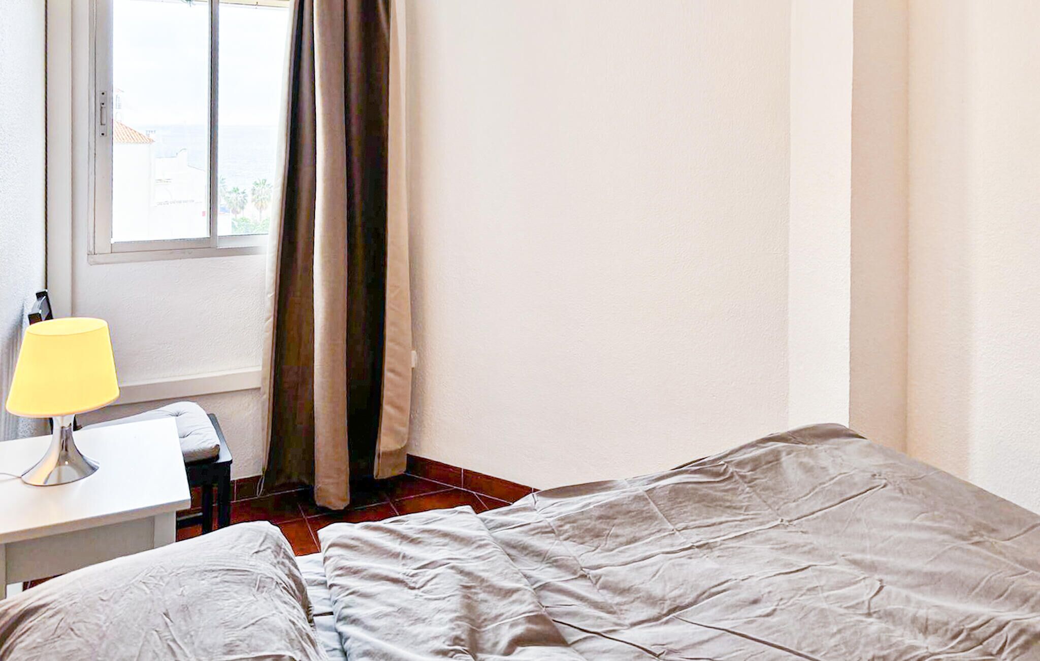 A bedroom with a bed, a desk, a lamp, and a window with curtains.
