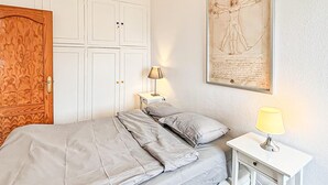Ein Schlafzimmer mit einem Bett, einem Nachttisch, einer Lampe, einem Holzschrank und einem gerahmten Bild an der Wand.