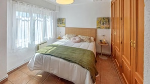 A bedroom with a bed, a bedside table, a lamp, a radiator, a window with curtains, and a wooden wardrobe. - House in Banyeres de Mariola (Banyeres de Mariola)