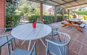 Un patio techado con una mesa redonda y sillas, una mesa de picnic de madera, y una taza roja sobre la mesa.